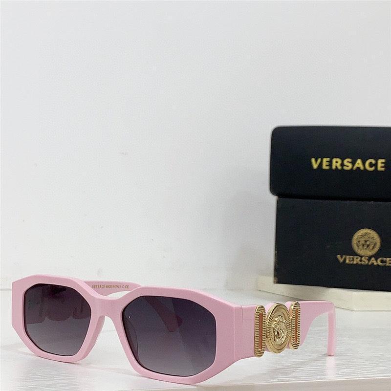 Pink designer sunglasses with gold medallion detail and dark lenses on white surface