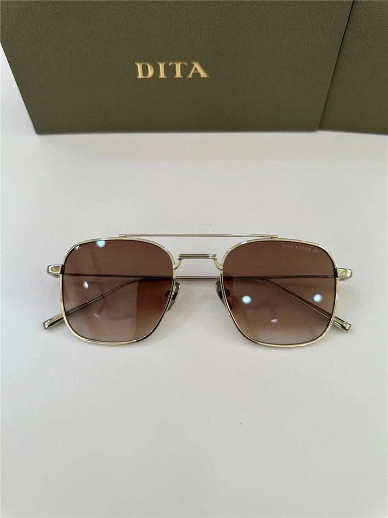 Gold frame aviator sunglasses with brown gradient lenses on white surface, DITA case background
