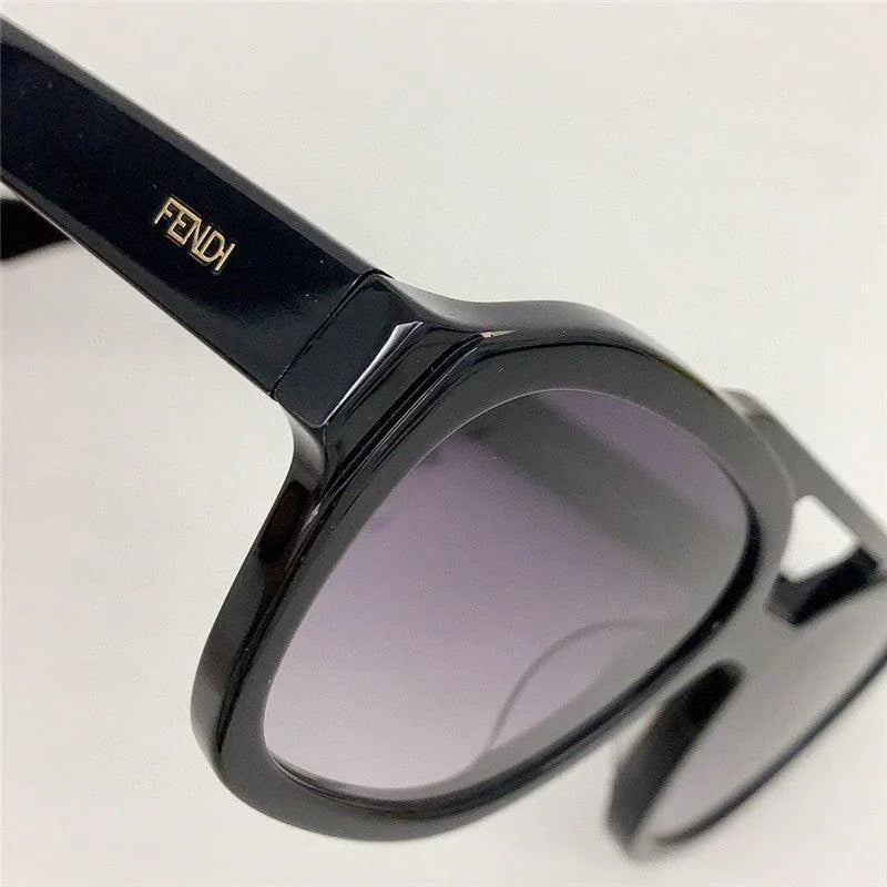 Black designer sunglasses with thick frames and gray gradient lenses on white background