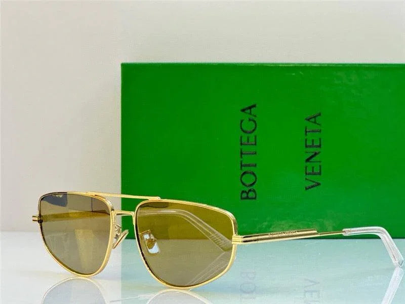 Gold aviator sunglasses with tinted lenses in front of a green designer box
