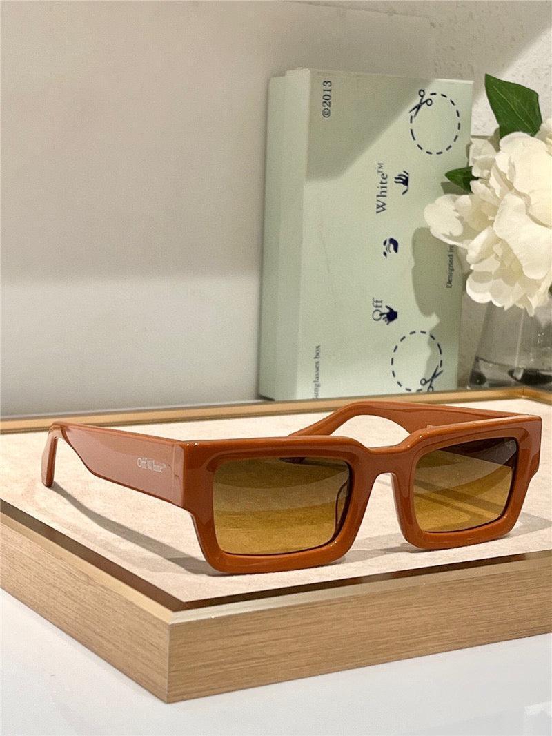 Rectangular brown sunglasses with amber lenses on a wooden tray, stylish eyewear display