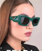 Woman wearing oversized green rectangular sunglasses with black lenses and gold chain necklace
