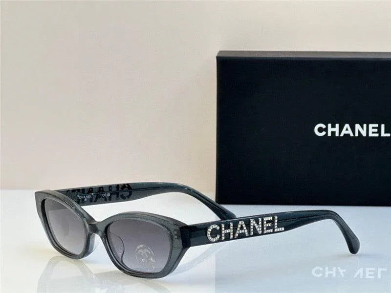 Black designer sunglasses with rhinestone CHANEL logo, dark lenses, box in background