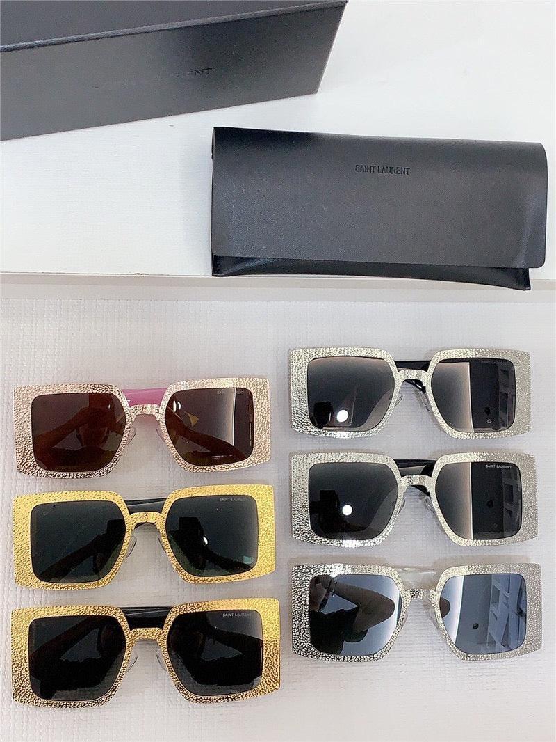 Six pairs of oversized square sunglasses with glitter frames in gold and silver, next to black Saint Laurent cases.