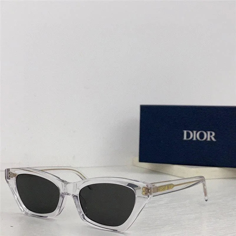 Clear cat eye sunglasses with dark lenses and gold accents on a white surface, Dior case in background