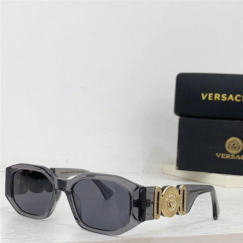 Black square sunglasses with gold medallion accents and dark lenses on a white surface