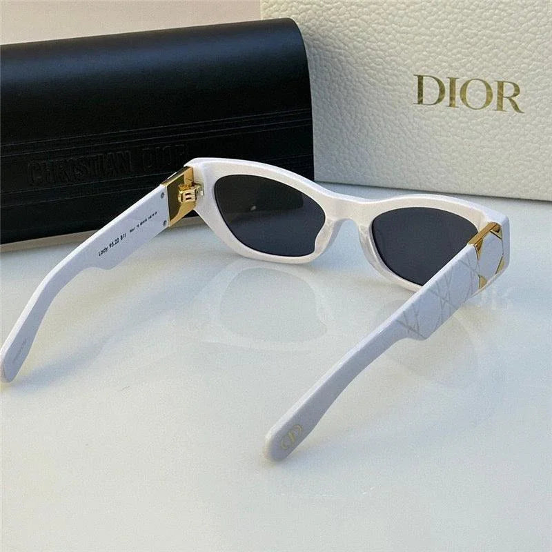 White cat-eye sunglasses with black lenses and gold accents, luxury designer style, on table