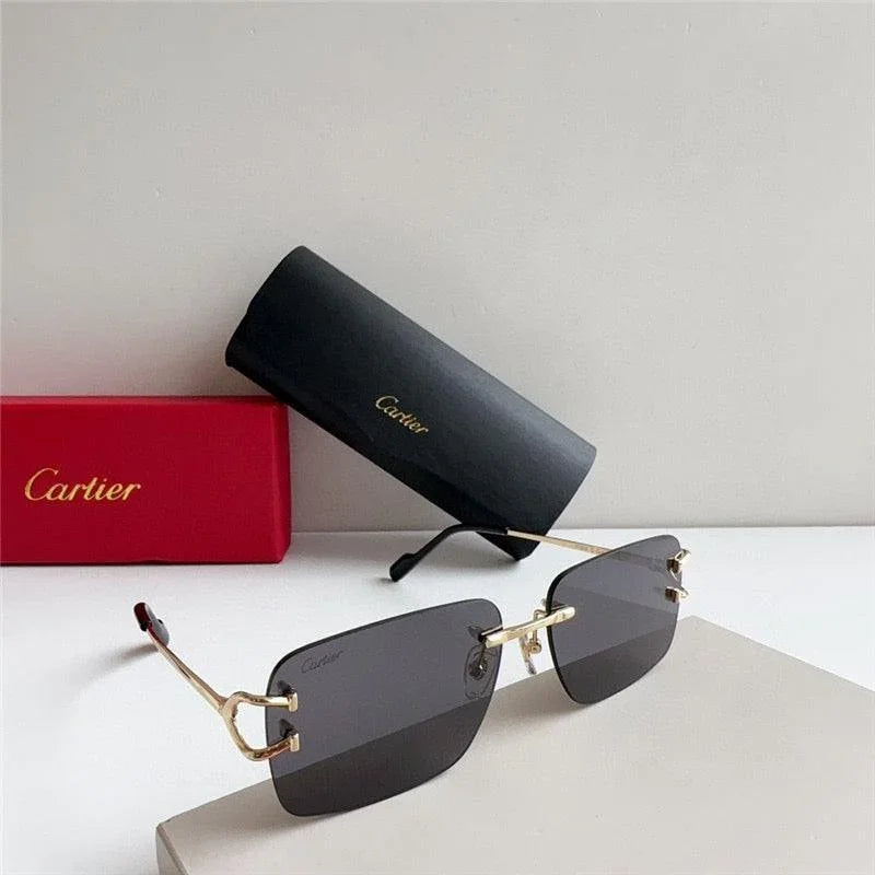 Rimless sunglasses with gold temples and dark lenses, black case and red box in background.