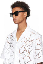 Man wearing black rectangular sunglasses and a white floral cut-out shirt, isolated background.