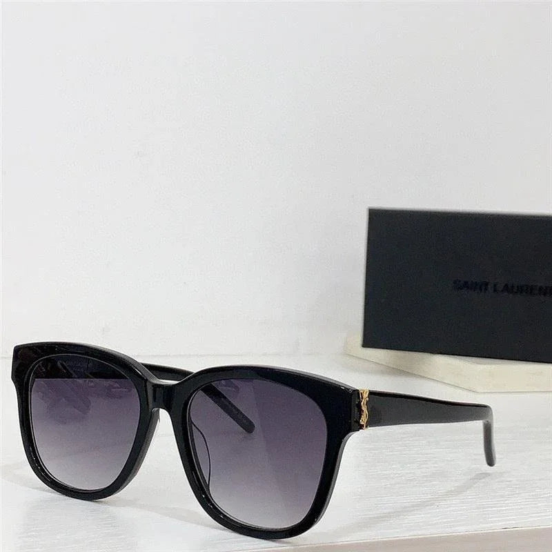 Black square sunglasses with gold accent and gradient lenses on white surface