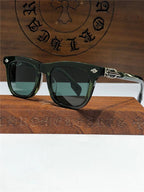 Black square sunglasses with silver accents, dark lenses, and designer details, displayed on a wooden box.