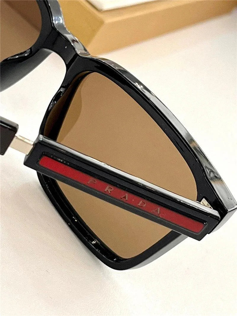 Black designer sunglasses with brown lenses and red-accented arms on a white surface