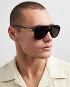 Man wearing black designer aviator sunglasses with gold accents and brown lenses