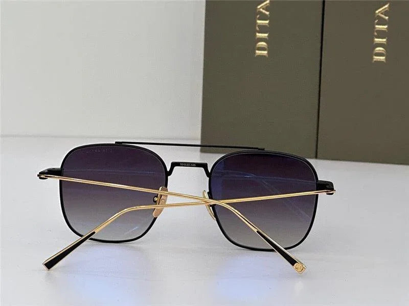 Black and gold square sunglasses with gradient lenses on white surface, two boxes in background