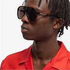 Man wearing oversized black sunglasses with dark lenses and a red collared shirt