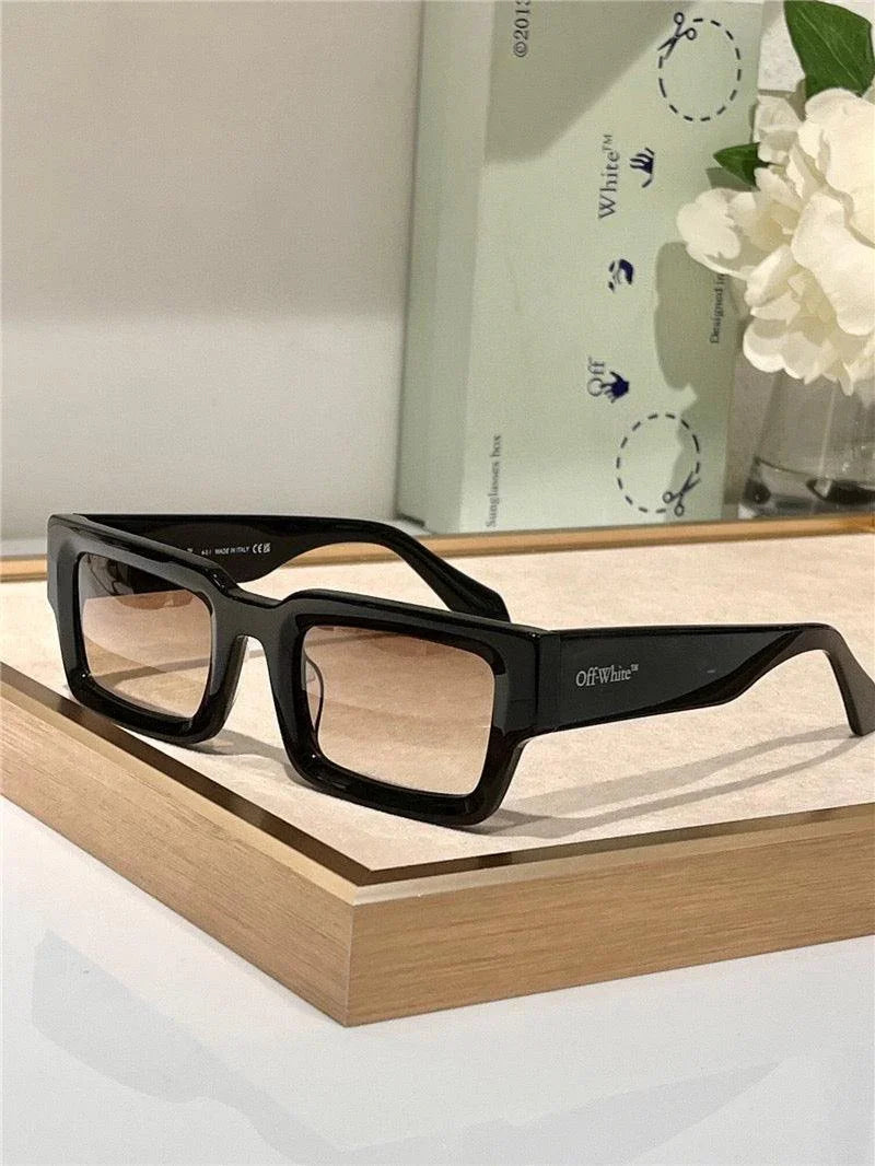 Rectangular black sunglasses with tinted lenses displayed on a light wood tray.