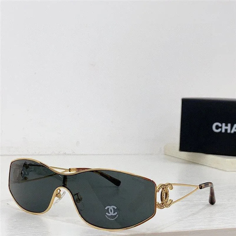 Oversized black sunglasses with gold wire frame and decorative side logo on a white shelf