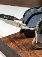 Close-up of luxury sunglasses with ornate metallic hinge and dark lenses on wooden surface