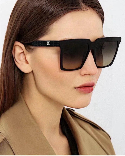 Woman wearing oversized square black sunglasses with gradient lenses and a tan coat