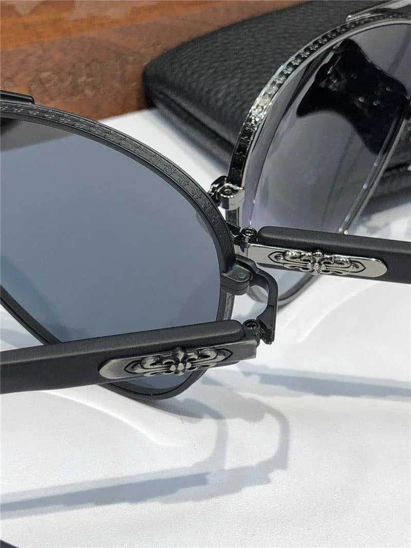 Close-up of stylish sunglasses with dark lenses and decorative temple details on a white surface.