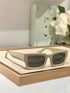 Beige rectangular sunglasses with thick frames and dark lenses on display, modern setting