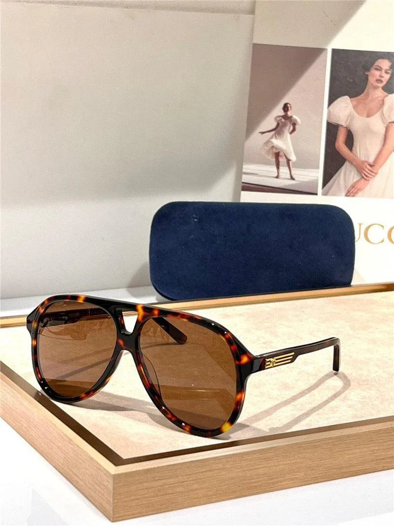 Tortoiseshell aviator sunglasses with brown lenses displayed on a beige tray, with a navy case in the background.