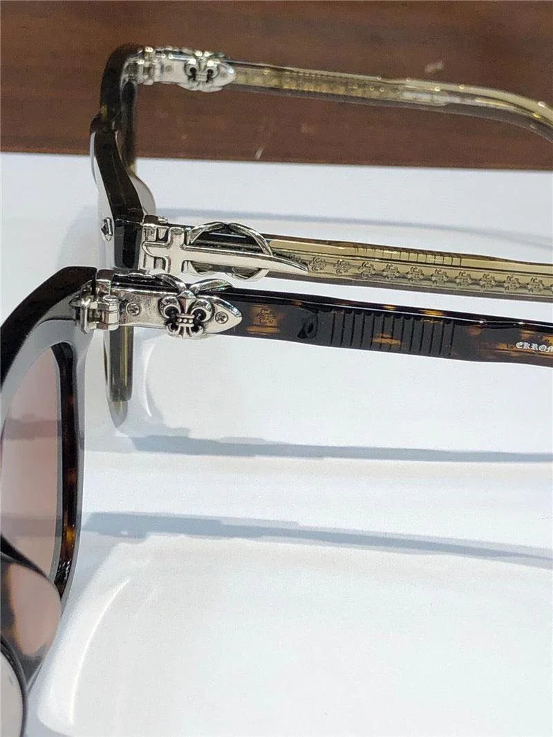 Close-up of luxury sunglasses arms with silver fleur-de-lis accents and tortoise frames.