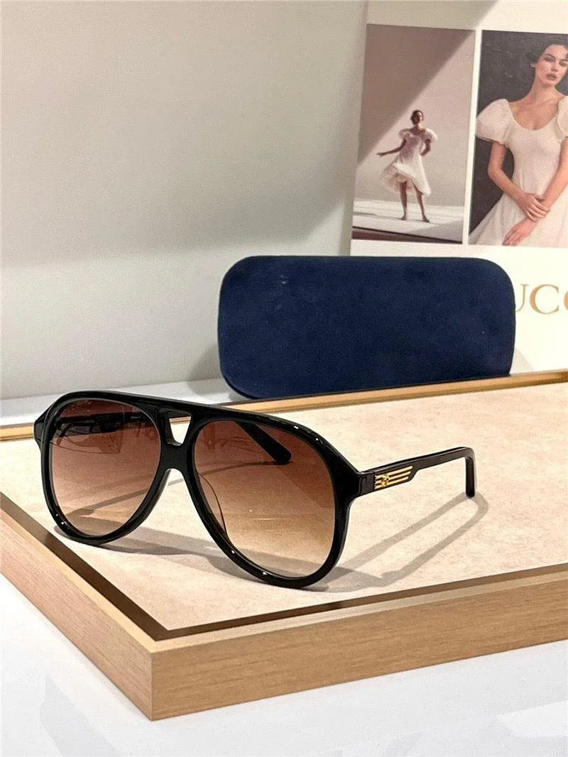 Black aviator sunglasses with brown gradient lenses and gold accents, displayed on a tray