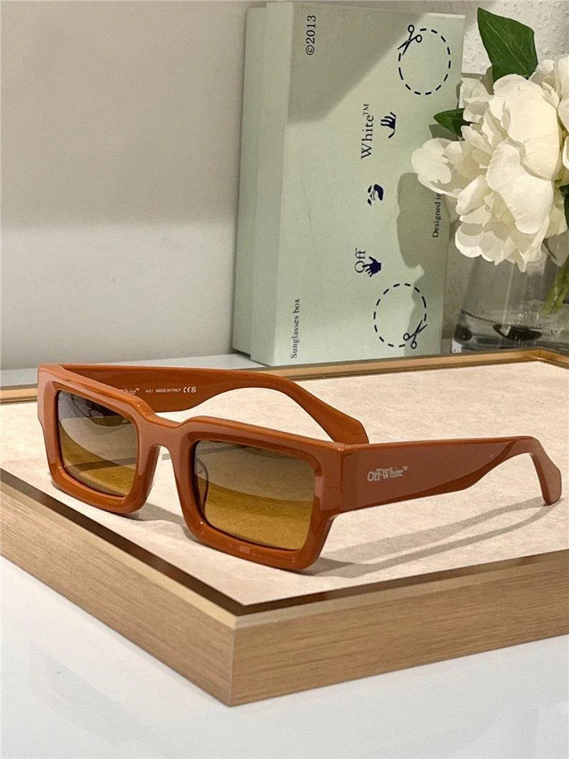 Square brown sunglasses with yellow-tinted lenses and bold frames on display tray